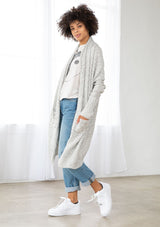 [Color: Silver/Ivory] A model wearing a silver grey knit reversible cardigan. With long sleeves, a waterfall open front, side pockets, and a shawl collar. 