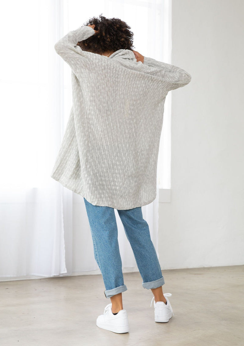 [Color: Silver/Ivory] A model wearing a silver grey knit reversible cardigan. With long sleeves, a waterfall open front, side pockets, and a shawl collar. 