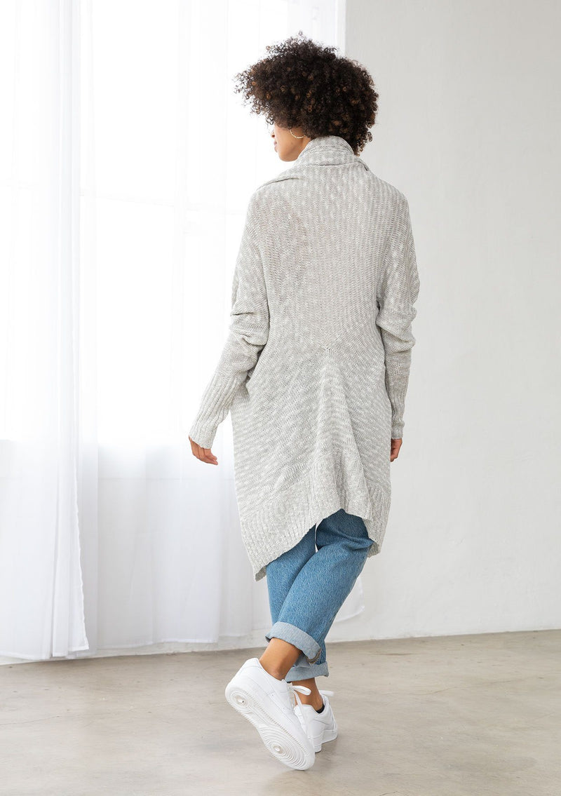 [Color: Silver/Ivory] A model wearing a silver grey knit reversible cardigan. With long sleeves, a waterfall open front, side pockets, and a shawl collar. 