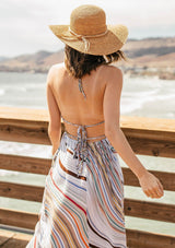 [Color: Earth Combo] A model wearing a multi color halter maxi dress in a wavy stripe print. With an open back and double strap tie, plunging v neckline, and side pockets. 