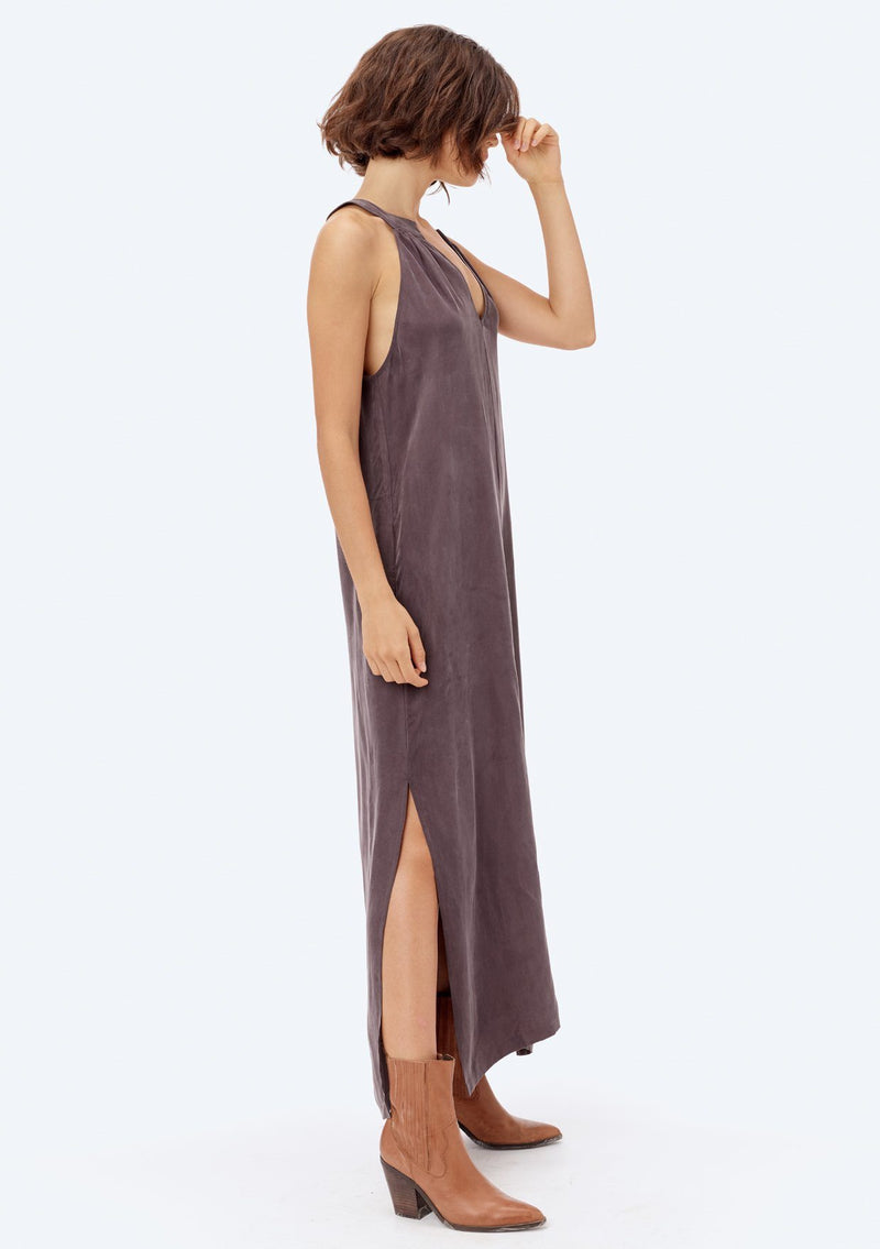 [Color: Charcoal] A brunette model wearing a cupro maxi dress with a split v-neckline, side pockets, and side slits. 