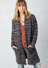 [Color: Heather Charcoal/Brown] A blonde model wearing a grey and brown melange stripe cardigan. Featuring a cozy shawl collar and front patch pockets. Perfect for casual fall outings. 