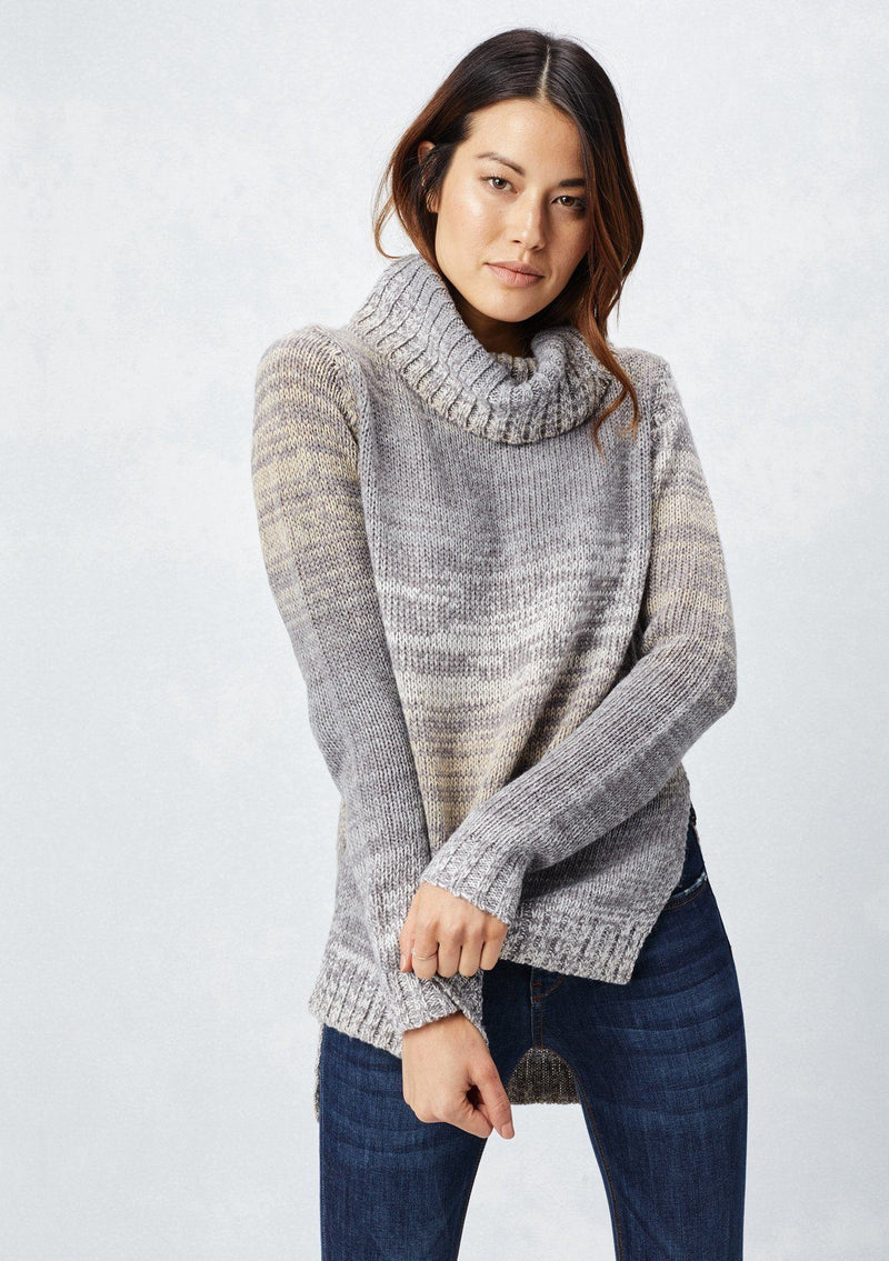 [Color: Grey/Cream] A brunette model wearing a space dye long sleeve sweater with a slouchy turtle neck, ribbed high low hem, and side vents. A cozy fall knit sweater for casual outings and cooler temperatures. 