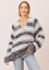 [Color: Black/White/Dove] A model wearing a cozy  slouchy, oversized fuzzy sweater. Featuring a deep v neckline and black, grey and white stripes. Perfect for fall styling. 