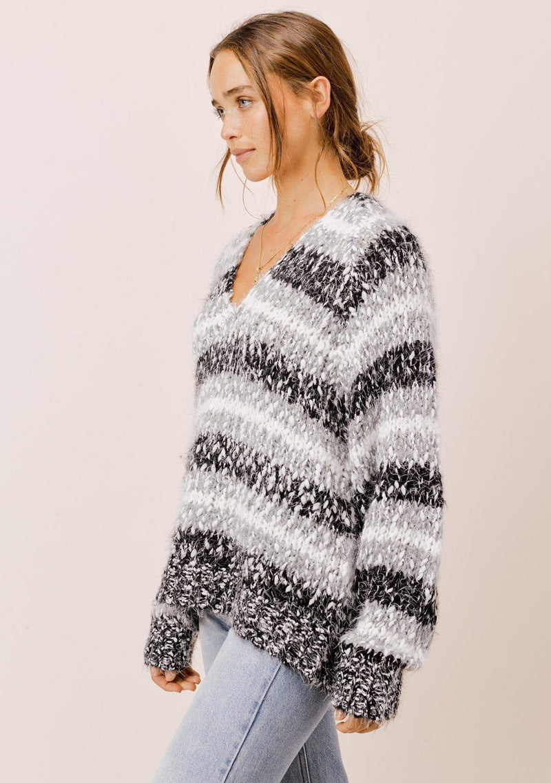 [Color: Black/White/Dove] A model wearing a cozy  slouchy, oversized fuzzy sweater. Featuring a deep v neckline and black, grey and white stripes. Perfect for fall styling. 