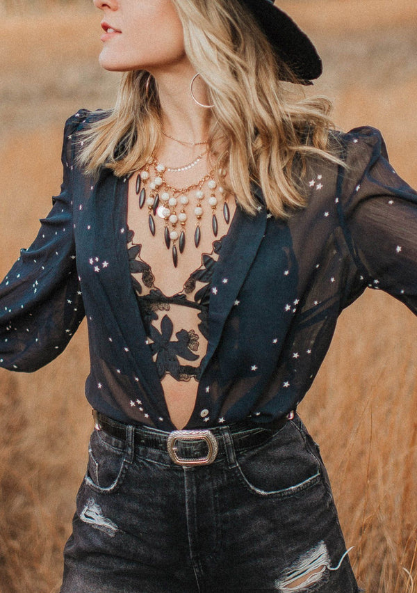 [Color: Midnight/Ivory] A blond woman wearing a sheer star printed button up shirt with volume sleeves and shirring detail, holding a disco ball.