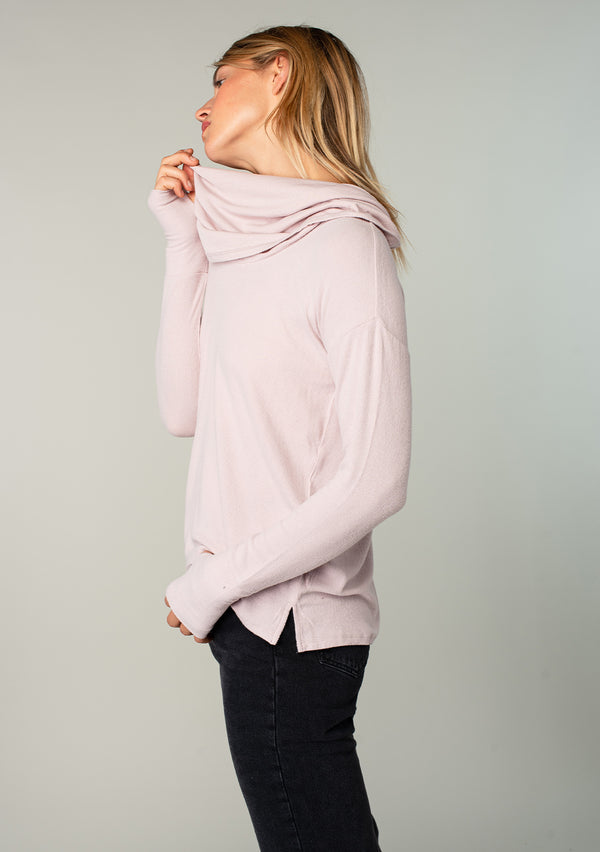 [Color: Dusty Rose] A model wearing a soft bamboo micro rib long sleeve top. Featuring an exaggerated cowl neckline that doubles as a hood, long sleeves with thumbhole accents, and breezy side vents.