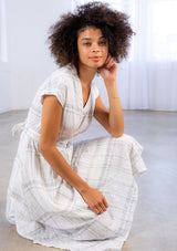 [Color: Ivory/Black] A model wearing a lightweight gauze, plaid wrap dress with tie back detail and handkerchief hem.