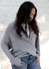 [Color: Heather Ash] A grey waffle knit cross front sweater. Featuring long dolman sleeves, a sexy cross front detail, and a flattering shawl collar that can be worn off the shoulder. Paired here with denim for a classic and chic Fall look. 