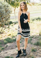 [Color: Black] A racerback mini dress with a drawstring neckline, embroidered details, and layered fringe hemline. 