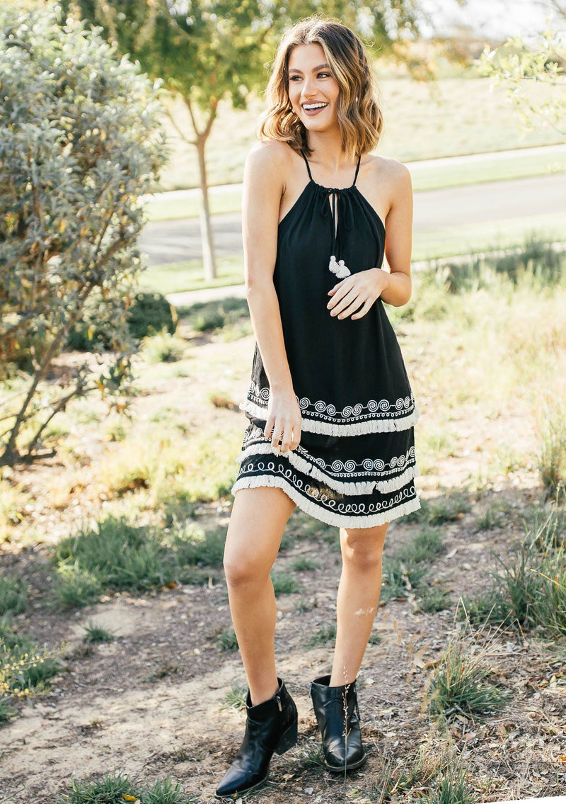 [Color: Black] A racerback mini dress with a drawstring neckline, embroidered details, and layered fringe hemline. 