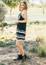 [Color: Black] A racerback mini dress with a drawstring neckline, embroidered details, and layered fringe hemline. 