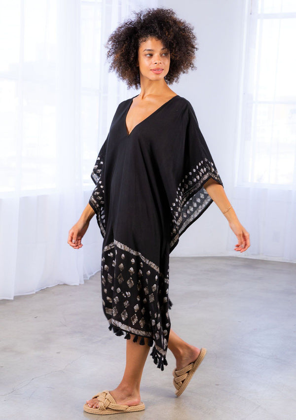 [Color: Black] A model wearing a block print caftan. With a v neckline in front and back and a tassel trim. 