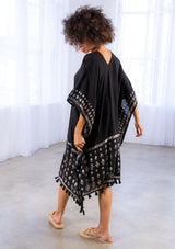 [Color: Black] A model wearing a block print caftan. With a v neckline in front and back and a tassel trim. 