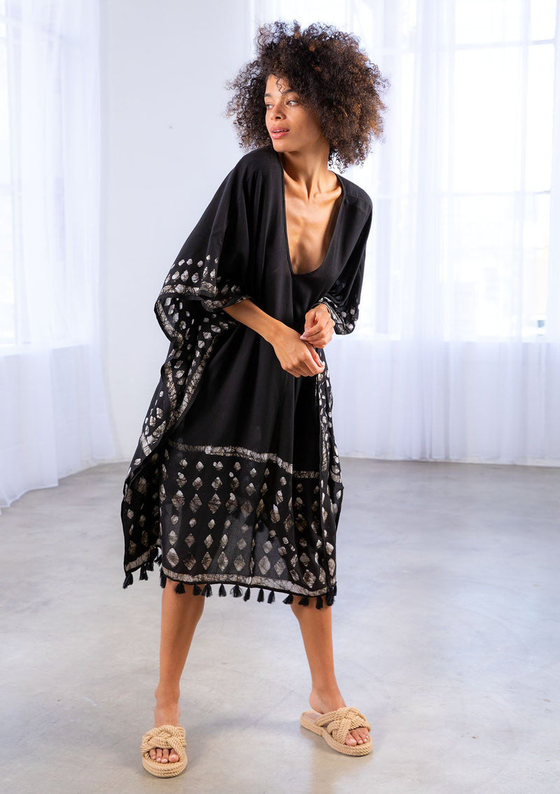 [Color: Black] A model wearing a block print caftan. With a v neckline in front and back and a tassel trim. 