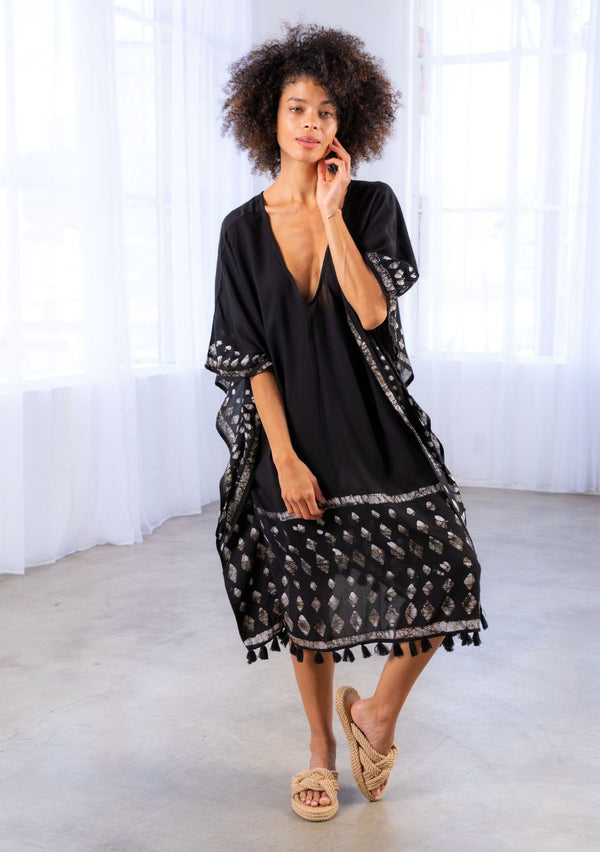 [Color: Black] A model wearing a block print caftan. With a v neckline in front and back and a tassel trim. 