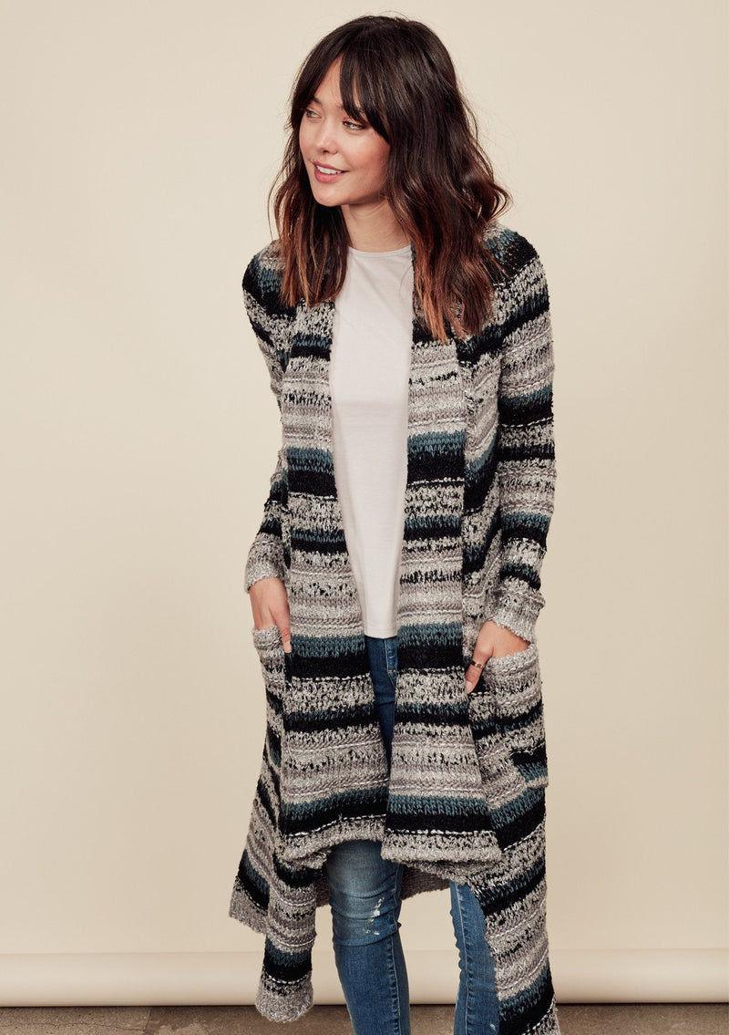 [Color: Grey/Teal/Black]  A front facing image of a brunette model wearing a bohemian striped knit duster cardigan in grey and blue with a shawl collar, side pockets, and a cozy, draped fit perfect for layering over denim.