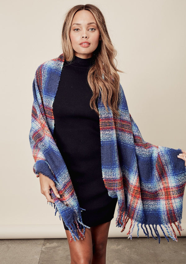 [Color: Blue Multi] a brunette model wearing a red and blue brushed boucle plaid scarf with a fringed trim. Perfect for cozy fall and winter days. 