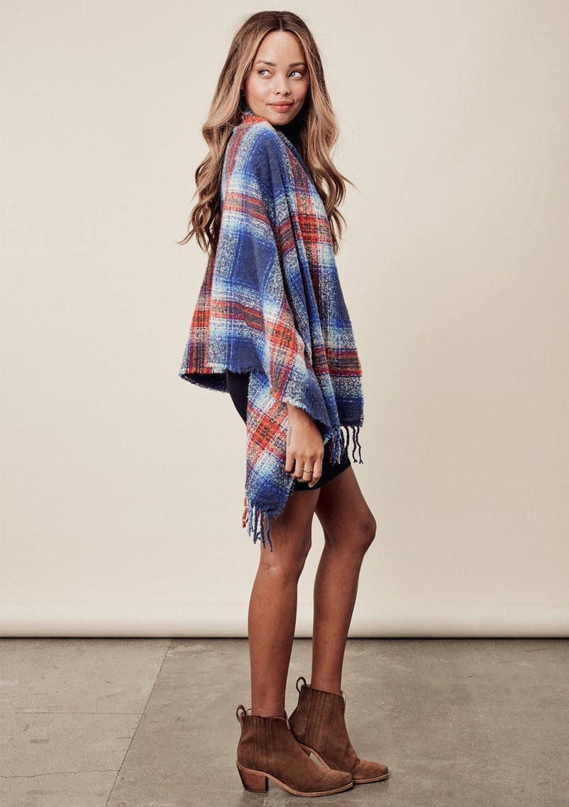 [Color: Blue Multi] a brunette model wearing a red and blue brushed boucle plaid scarf with a fringed trim. Perfect for cozy fall and winter days. 